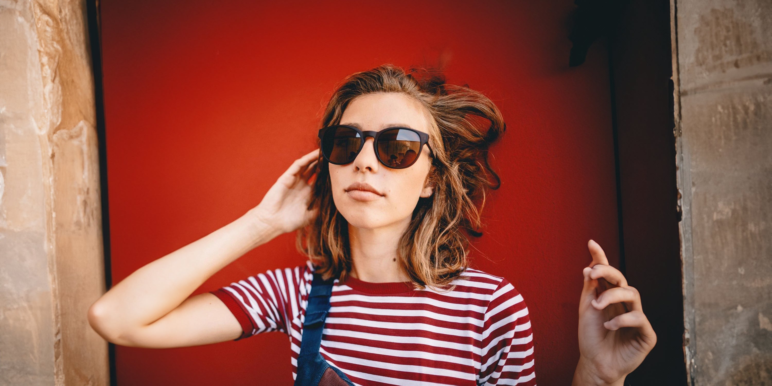Junge Frau trägt Take A Shot Sonnenbrille vor rotem Hintergrund - Desktop.webp