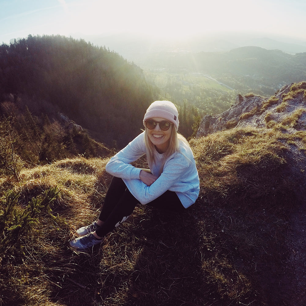 Junge Frau sitzt in der Natur und trägt eine Take A Shot Sonnenbrille