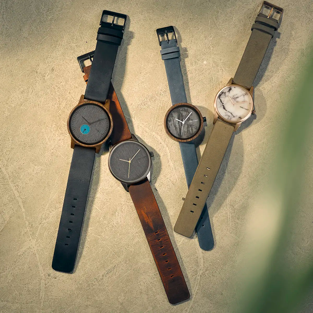 Mehrere nachhaltige Armbanduhren von Take A Shot liegen auf hellem Untergrund