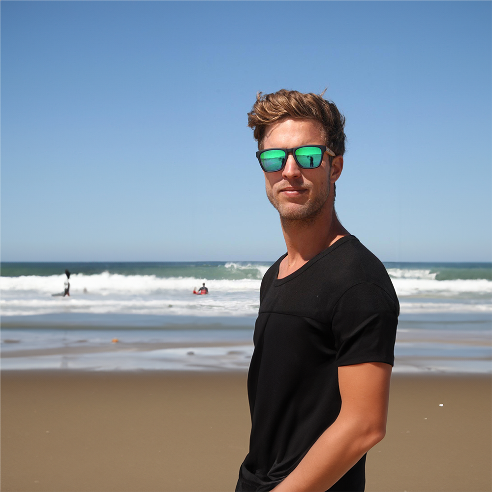 Junger Mann trägt eine Take A Shot Sonnenbrille am Strand